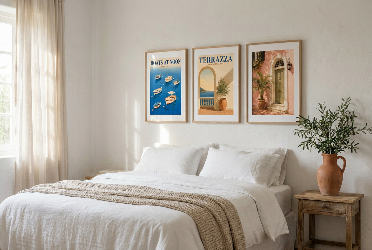 Three Mediterranean prints in wood frames above a white linen bed with an olive branch on the nightstand